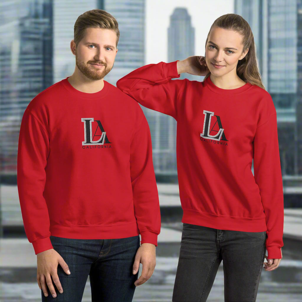 Two people wearing red sweatshirts with black and white letters. L.A. logo. Short for Los Angeles. background is city with five skyscrapers.