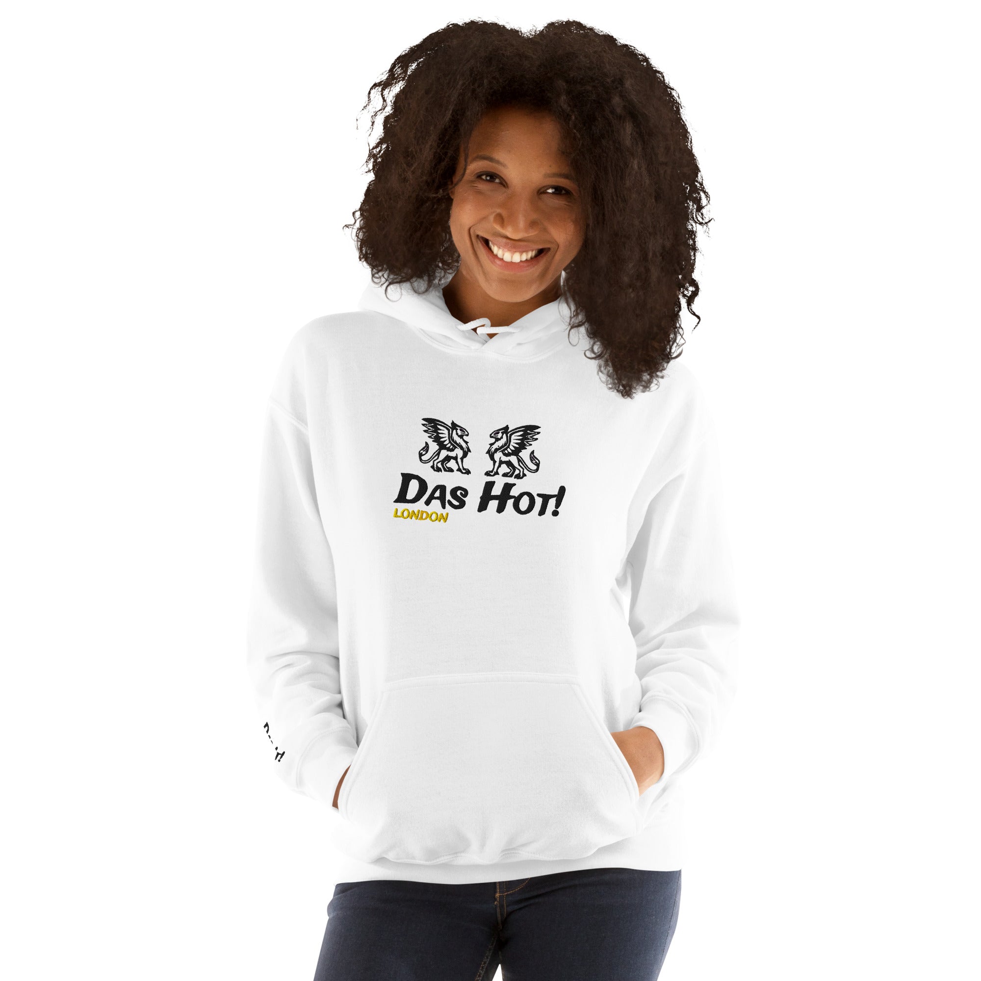 Front view of a smiling female model with curly hair showcasing the premium white unisex streetwear hoodie by Das Hot! London. The chest features high-density black raised embroidery of twin heraldic griffins and the Das Hot! brand name with a contrasting yellow-gold embroidered London accent located directly underneath, while a small matching embroidered brand accent is visible on the lower right sleeve.