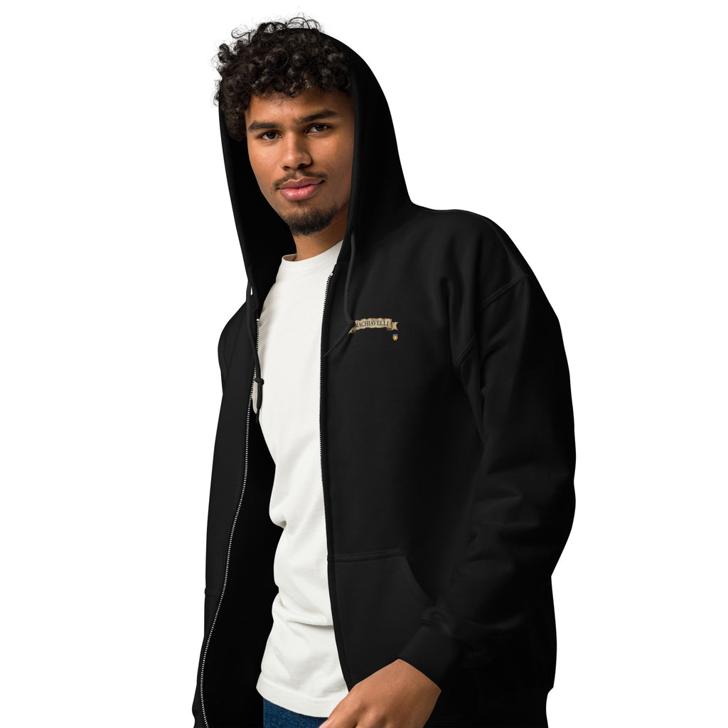 Cropped front view of a male model with a goatee wearing the premium black zip-up streetwear hoodie by Das Hot!. The hoodie is styled open over a plain white t-shirt, highlighting the silver metal zipper track and the left chest embroidery featuring the name MACHIAVELLI inside an antique parchment paper scroll banner design.