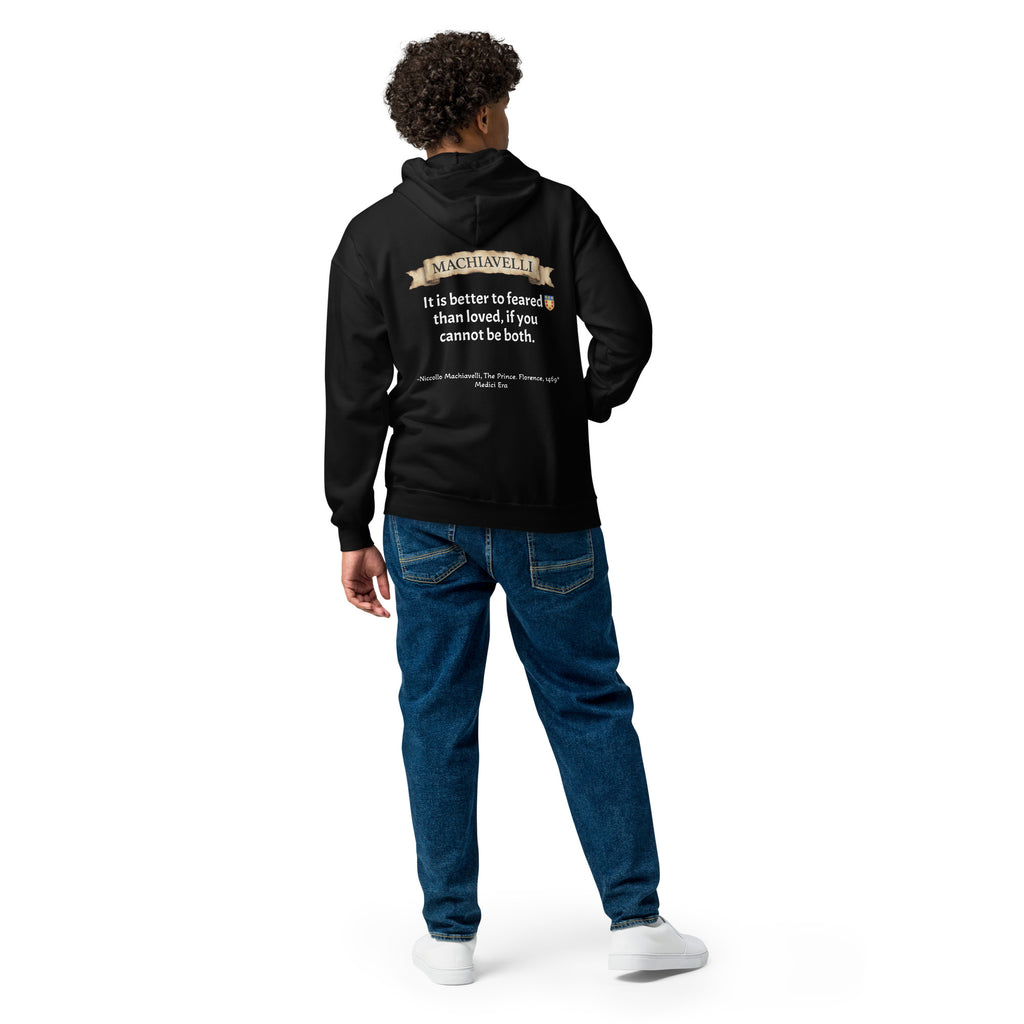 Rear view of a male model with dark curly hair posing in the premium black zip-up streetwear hoodie by Das Hot!. The hoodie is paired with blue jeans, showcasing the large back graphic that features the antique parchment paper scroll banner with the name MACHIAVELLI, his famous quote paired with the red-and-gold shield crest, and the historical citation text across the lower back against a white studio background.