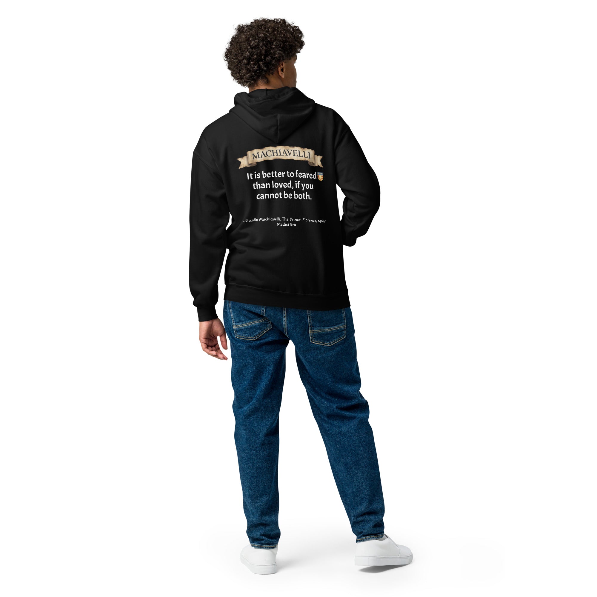 Rear view of a male model with dark curly hair posing in the premium black zip-up streetwear hoodie by Das Hot!. The hoodie is paired with blue jeans, showcasing the large back graphic that features the antique parchment paper scroll banner with the name MACHIAVELLI, his famous quote paired with the red-and-gold shield crest, and the historical citation text across the lower back against a white studio background.