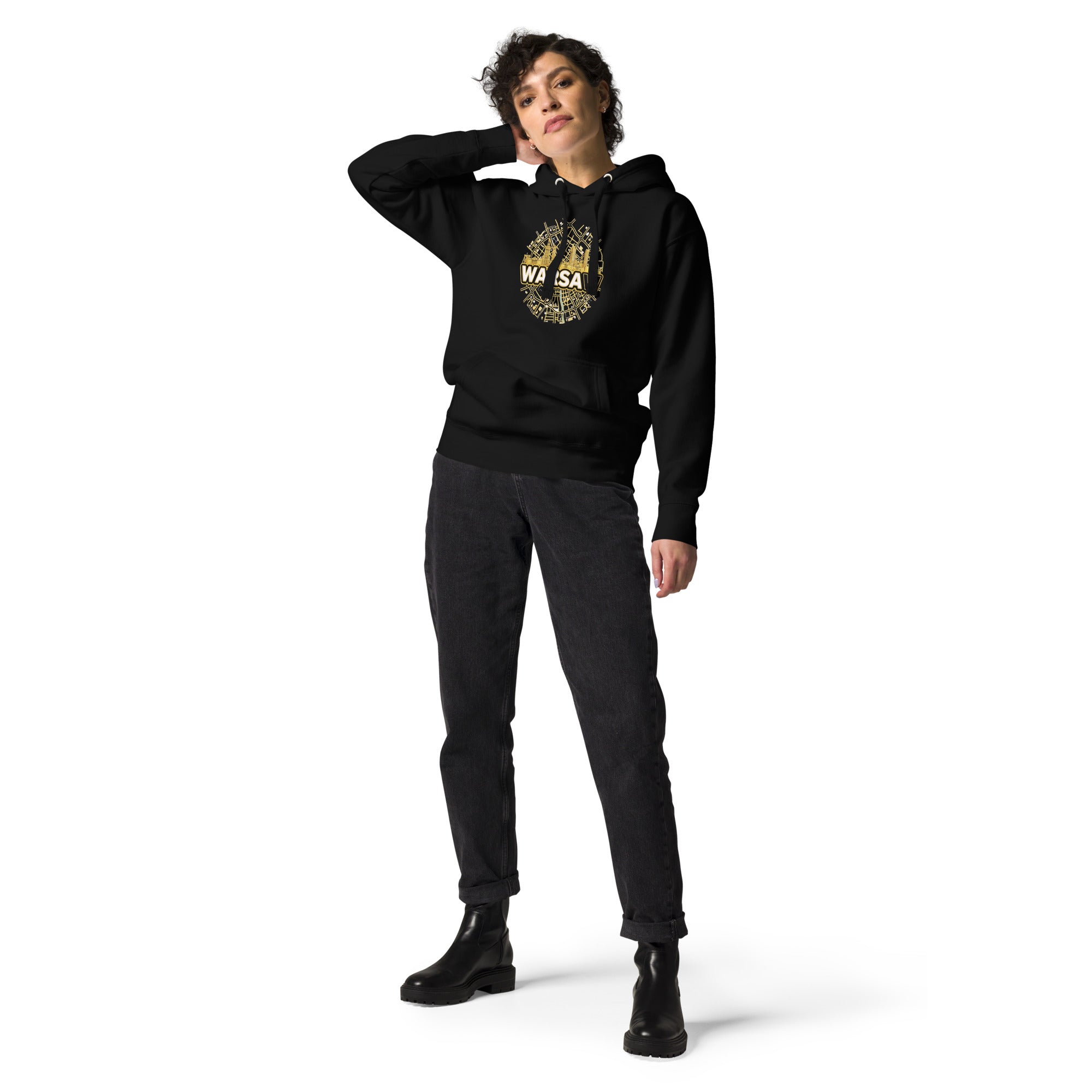 Full length view of a female model posing in the premium black unisex streetwear hoodie by Das Hot!. The outfit is paired with black jeans, showcasing the unisex fit and drape of the hoodie, which features the circular gold Warsaw city map and skyline chest graphic with white text.