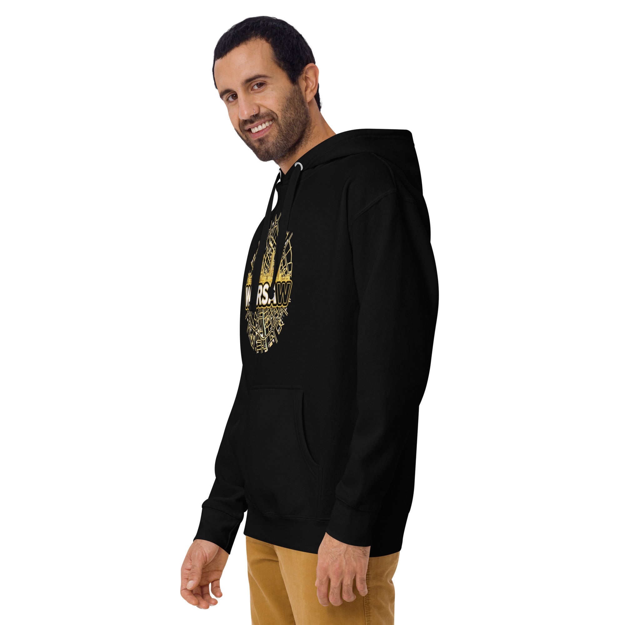 Side profile view of a smiling bearded male model looking back toward the camera, wearing the premium black unisex streetwear hoodie by Das Hot!. The angle showcases the fit of the sleeve and hood, while highlighting the side view of the circular gold Warsaw city map and skyscraper skyline chest graphic.