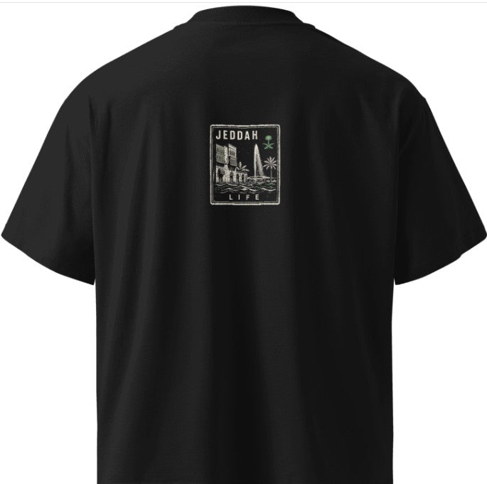Back of a black Das Hot! oversized streetwear T-shirt featuring the Das Hot! Passport™ Jeddah Life collectible badge with Al-Balad architecture, the Jeddah Fountain, palm trees, and Saudi-inspired artwork.