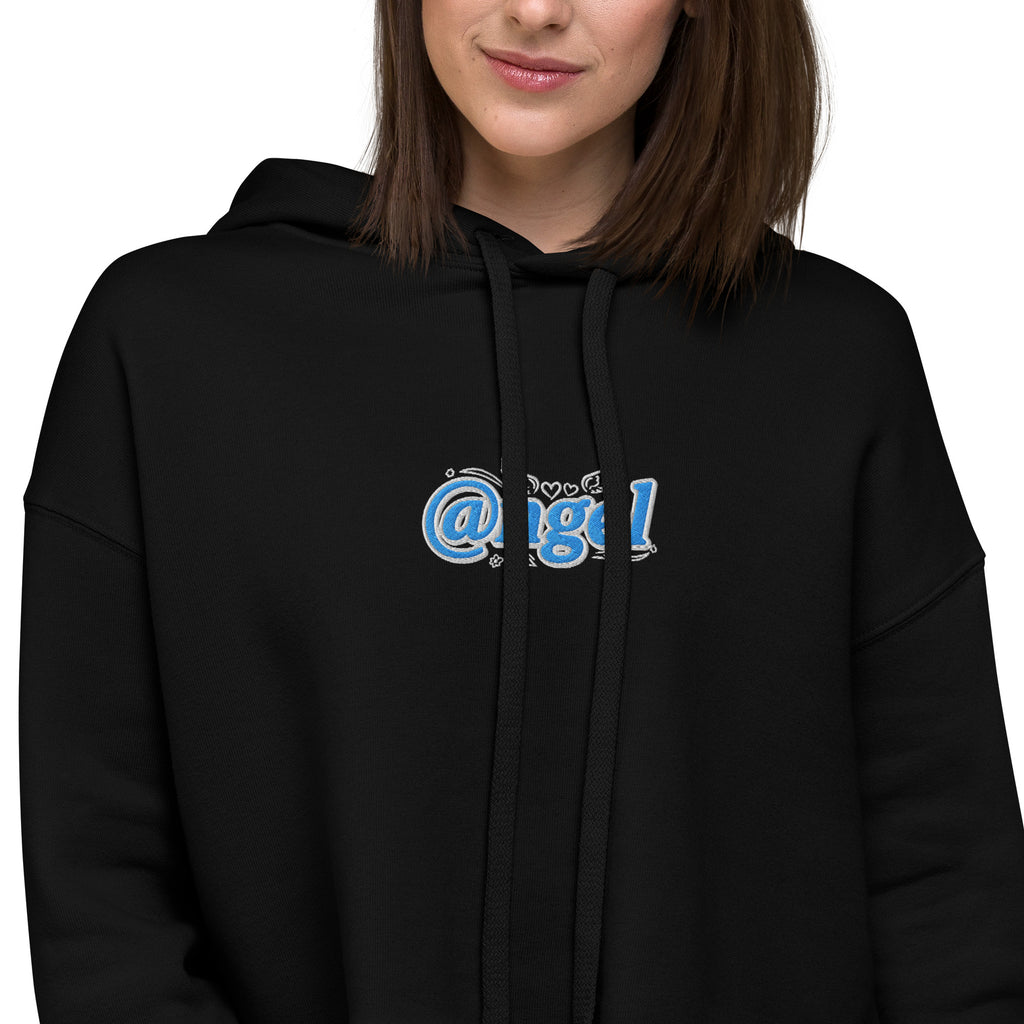 An extreme close-up detail view of the premium dual-tone light blue and white "@ngel" (Angel) graphic embroidery on the black Dashot cropped hoodie. The shot clearly showcases the high-density texture of the stitching, the signature "at" sign typography, tiny embroidered winged hearts, flat black drawstrings, and the fine weave of the midnight black fleece on a model.