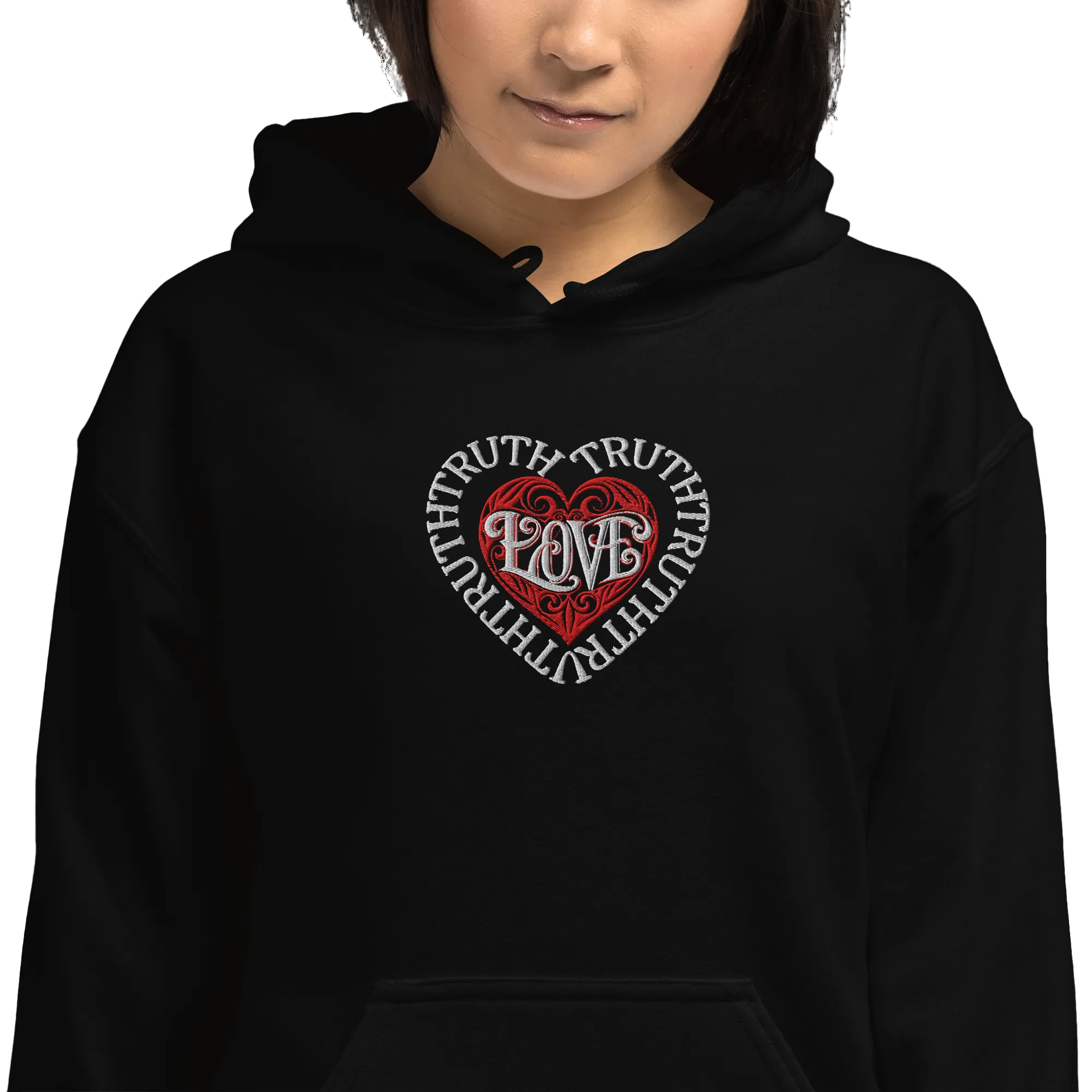 A chest-level view of a model wearing the solid black Dashot hoodie, emphasizing the premium texture of the embroidered chest graphic where a protective white heart formed by the word TRUTH shields a red tribal heart design containing the word LOVE.