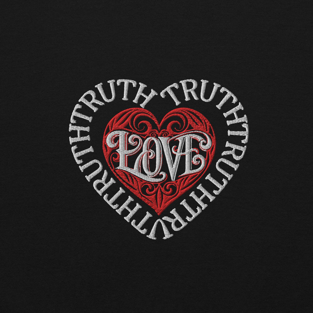 A direct macro texture view of the premium high-density chest embroidery on a black Dashot hoodie, showcasing the thick white stitched words of TRUTH forming a heart-shaped barrier wall around a red stitched tribal heart with the word LOVE woven at the center.