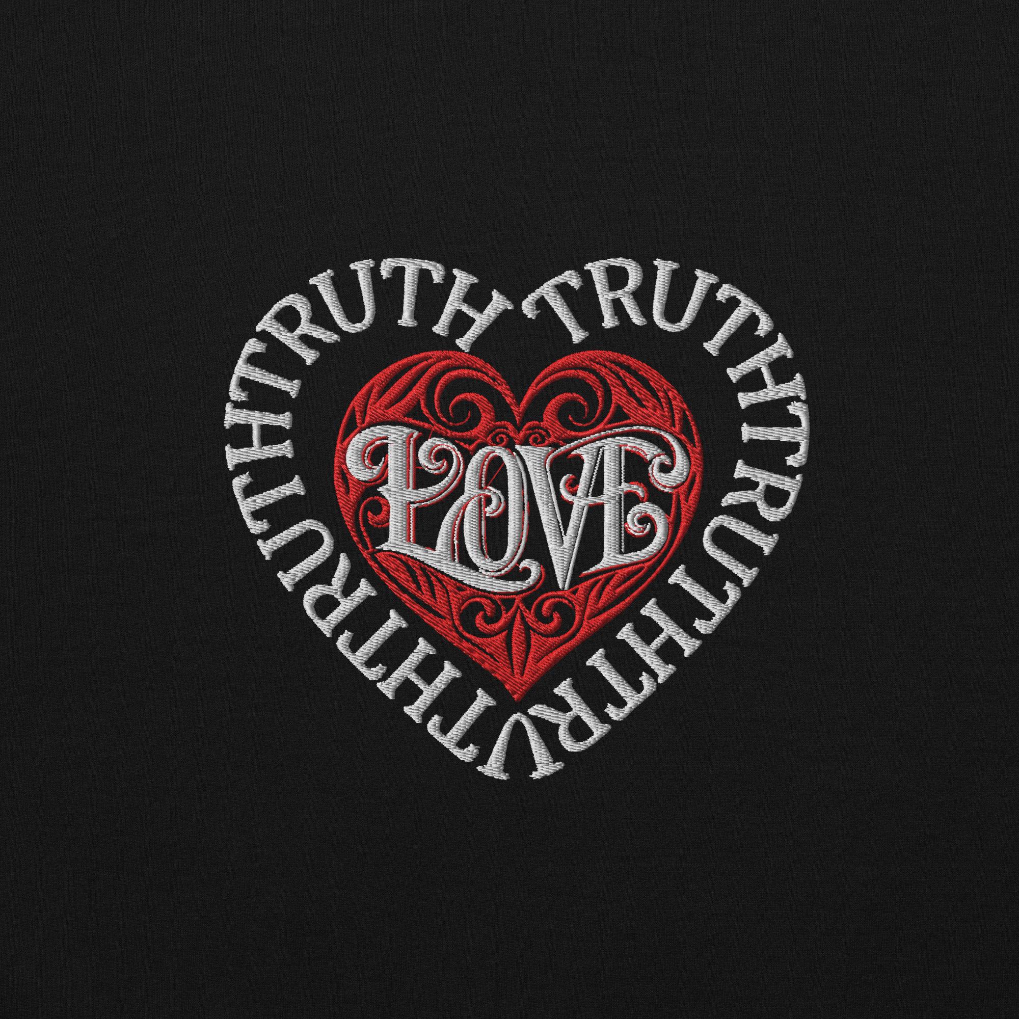 A direct macro texture view of the premium high-density chest embroidery on a black Dashot hoodie, showcasing the thick white stitched words of TRUTH forming a heart-shaped barrier wall around a red stitched tribal heart with the word LOVE woven at the center.