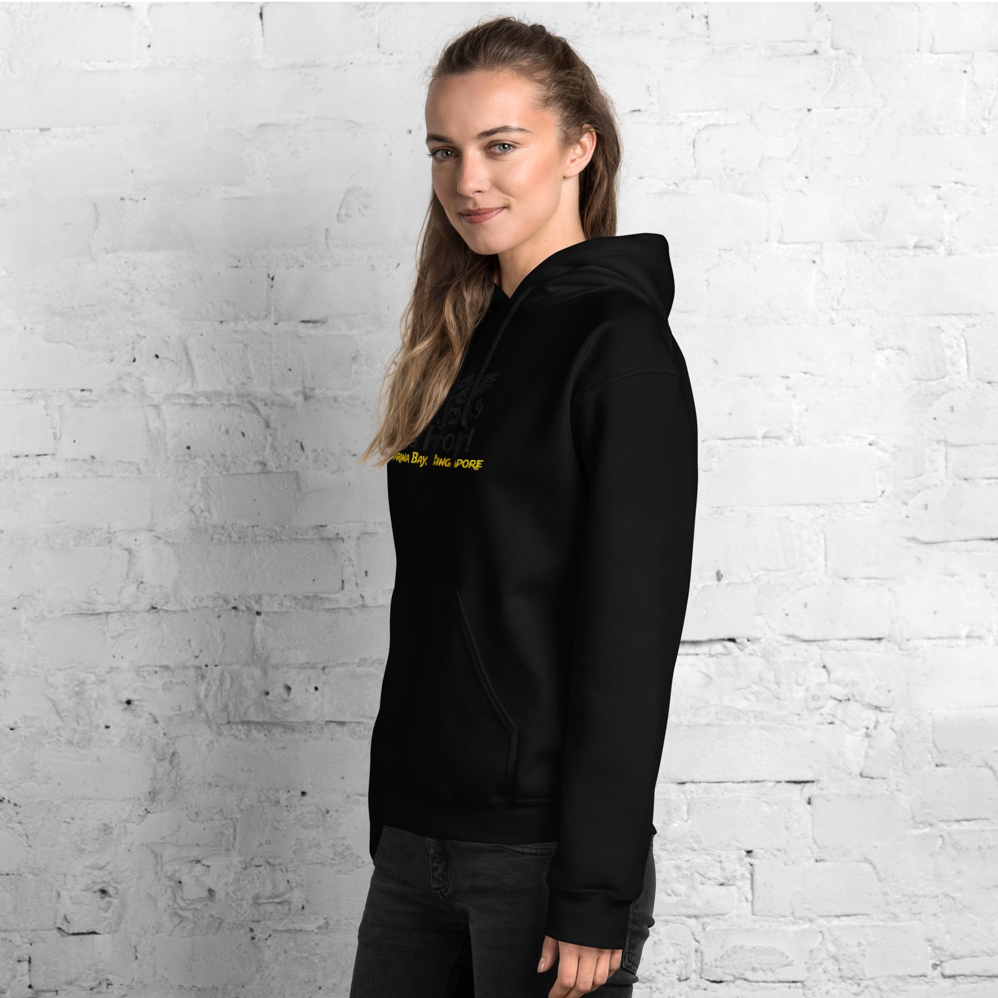 Person wearing a black hoodie with yellow text against a white brick wall