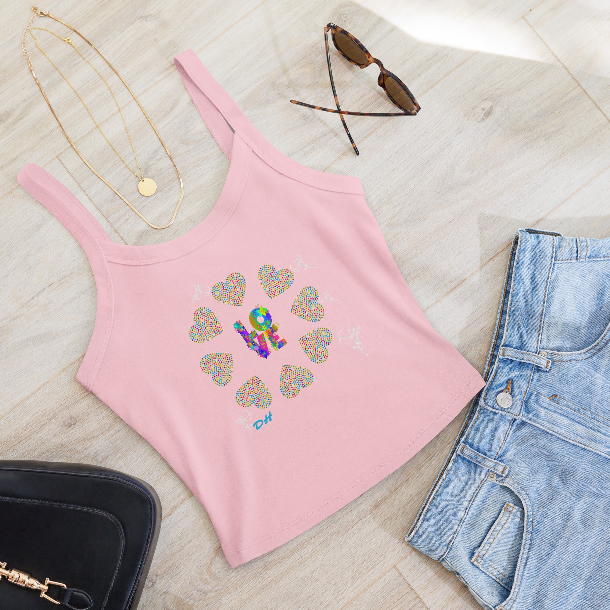 Pink tank top with colorful heart design, sunglasses, necklace, and jeans on a light wooden surface.